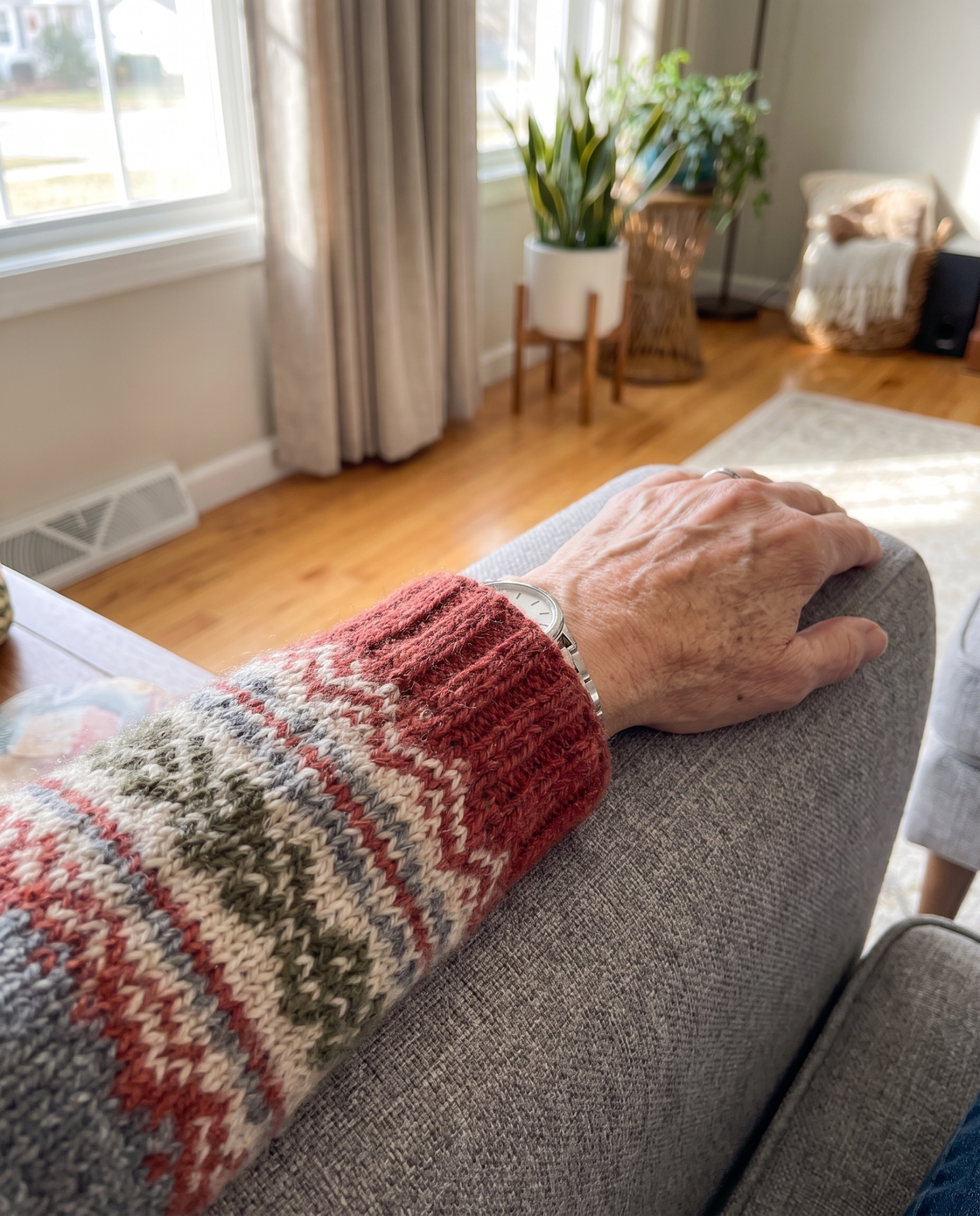 Close-up of a plush knit cardigan sleeve pushed up toward the elbow, resting on the arm of a chair