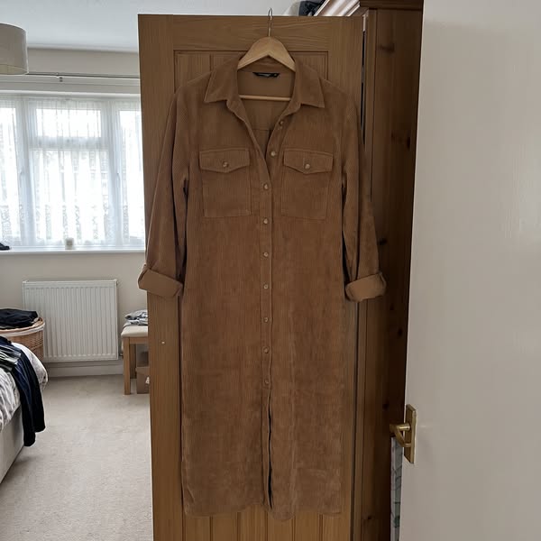 The Averlina dress on a hanger on a bedroom door, sleeves rolled, collar and button front visible