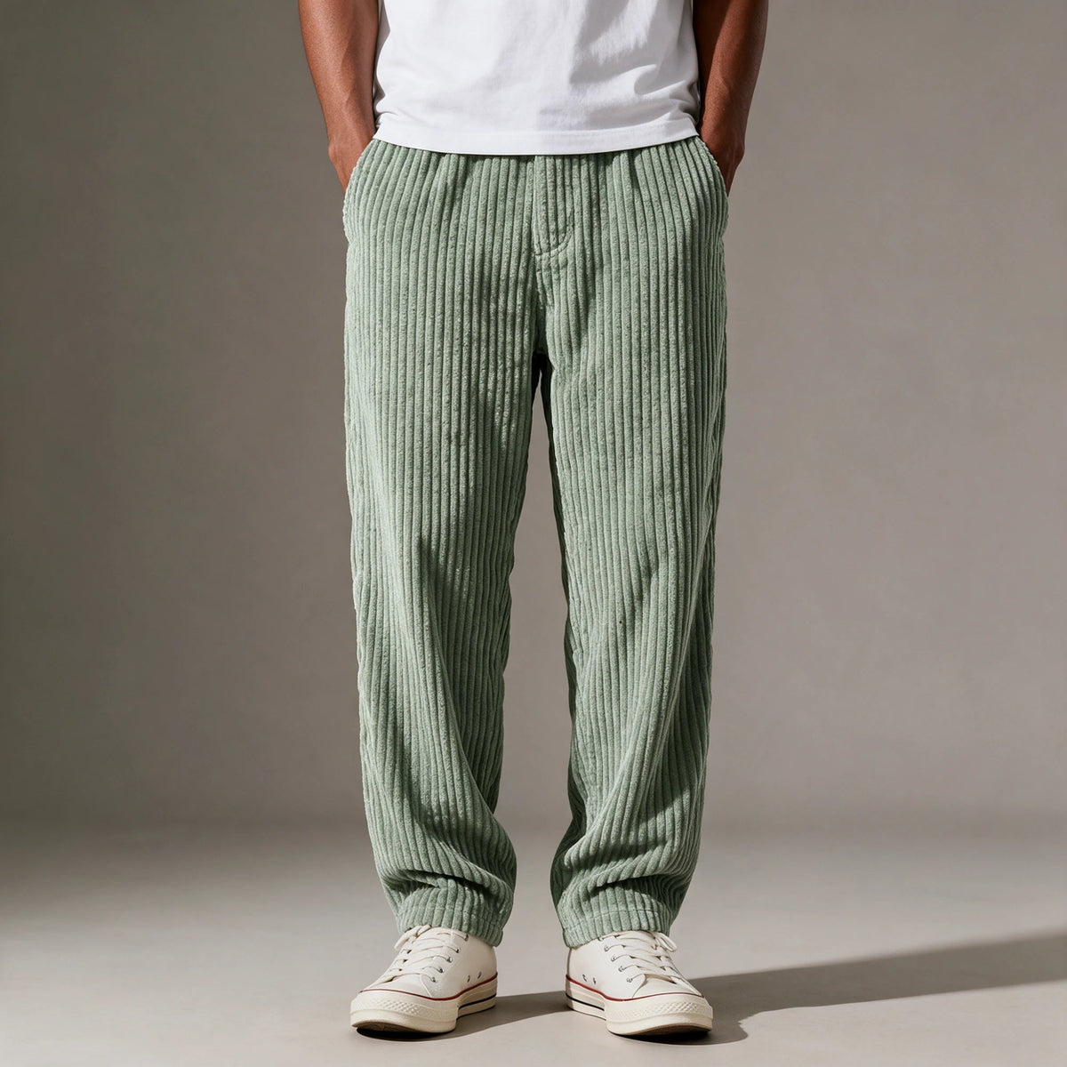 A man wearing the Clark pants in light green with a white T-shirt and white sneakers, front view, hands in his pockets.