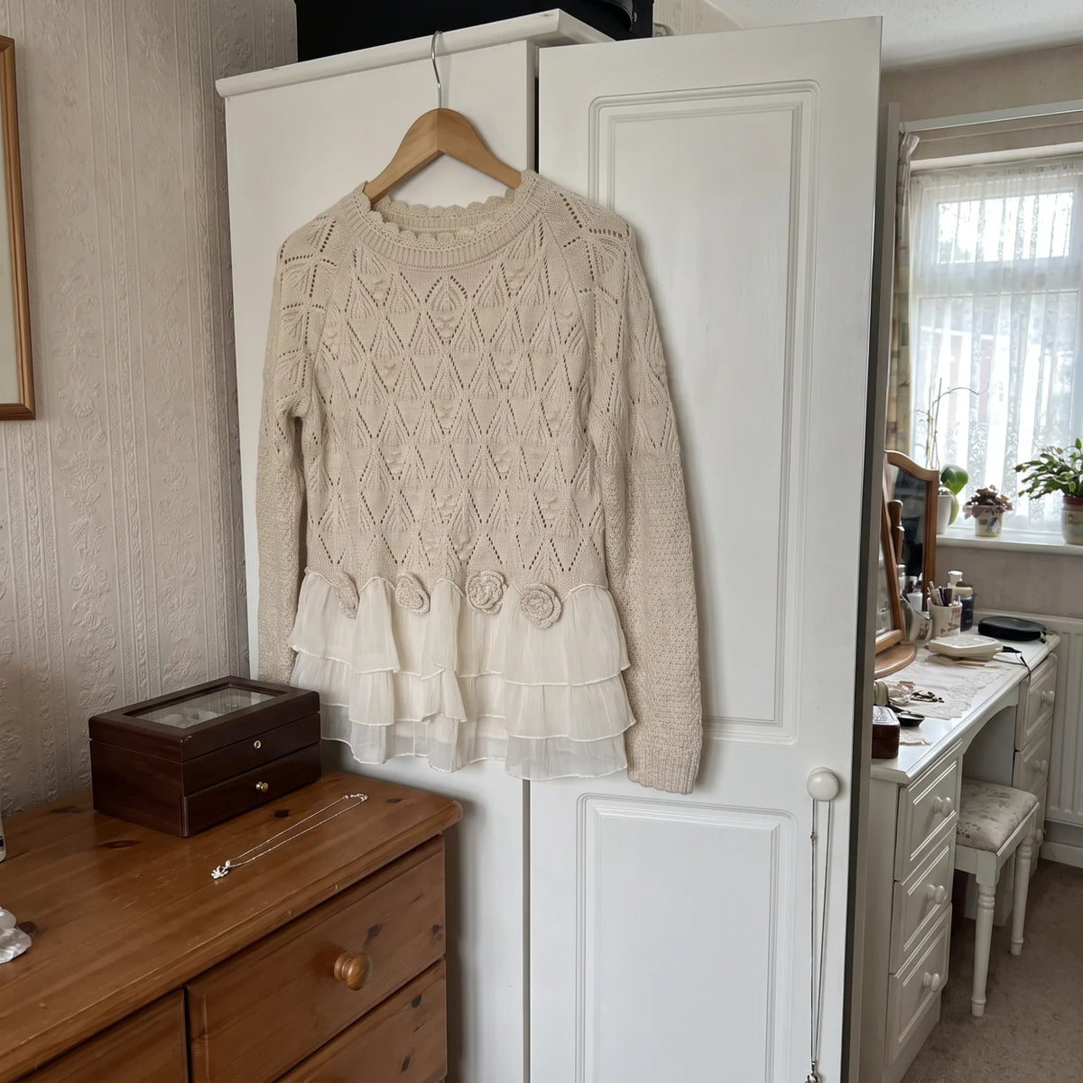 The Ruvella sweater on a hanger on the closet door, jewelry box and necklace below