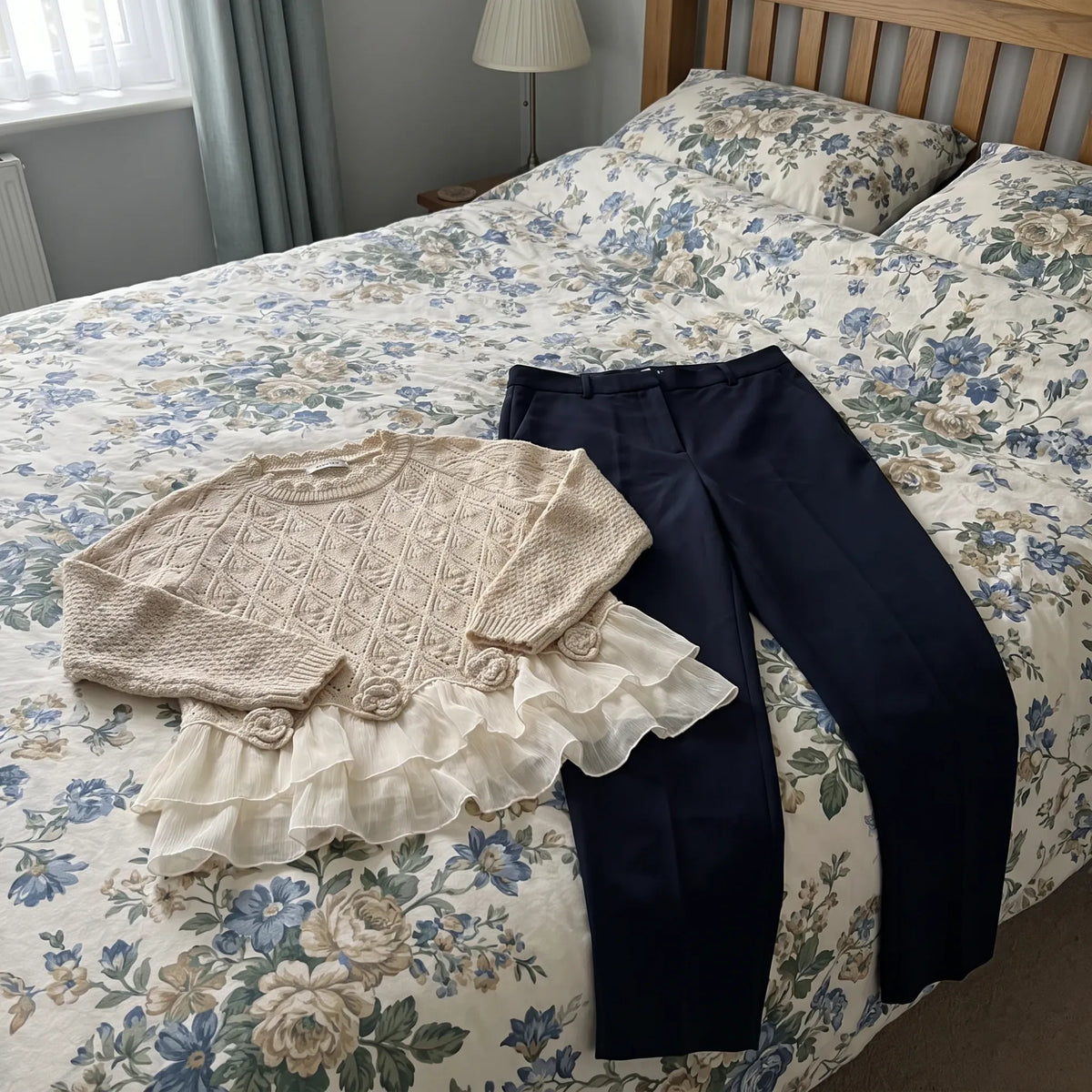 The Ruvella sweater laid out on the bed next to navy pants